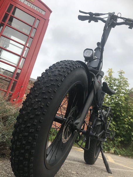 A foldable electric 20x4 fat tyre bike next to a UK telephone box
