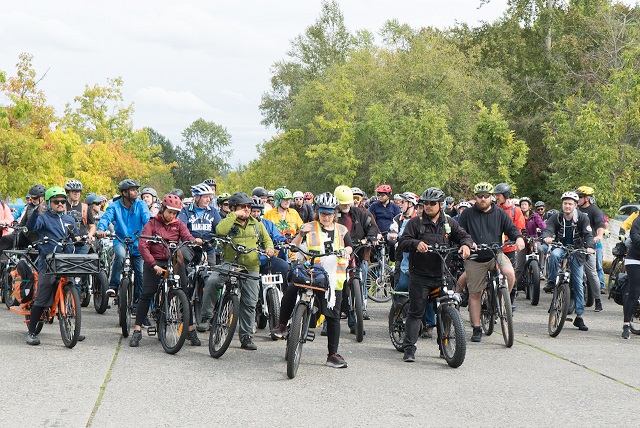 A huge group of diverse bikers on various types of electric bikes have gathered together for a ride.